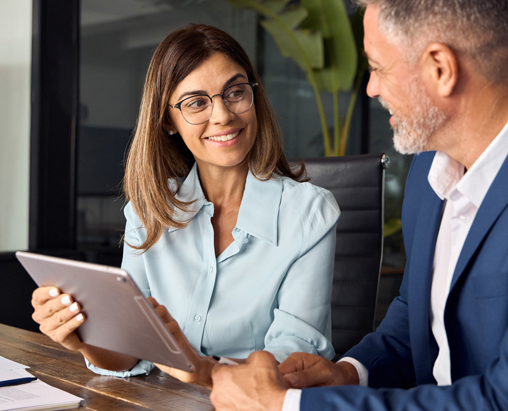 A woman and a man having a meeting in an office, woman holding a tablet and smiling.